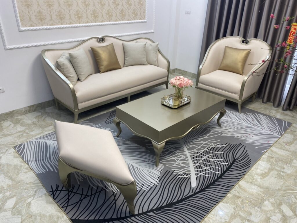 Armchair Daphne tân cổ điển bọc vải kem, khung bạch kim, đặt cạnh sofa Daphne, bàn trà và đôn ngồi trên thảm hoạ tiết lá
