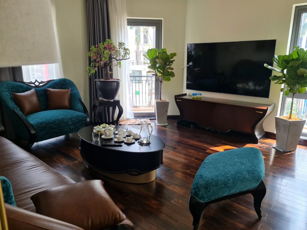 Phòng khách tân cổ điển sàn gỗ với kệ tivi Augustus màu nâu, armchair và đôn bọc nhung xanh