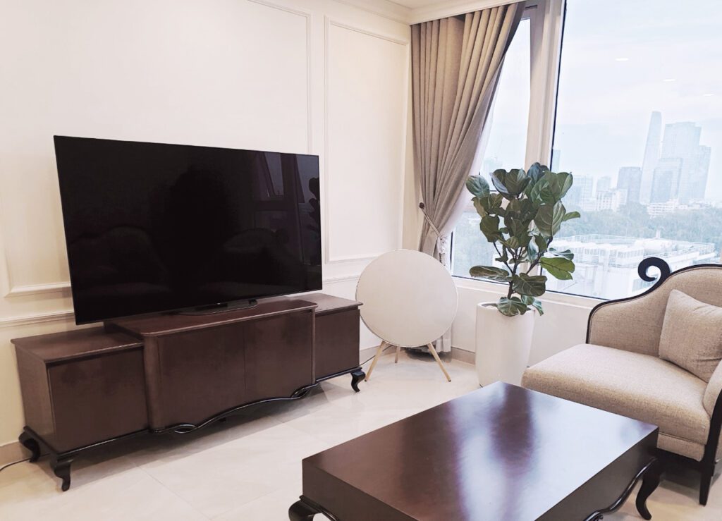 Kệ tivi Daphne tân cổ điển màu nâu đặt dưới TV lớn trong phòng khách căn hộ