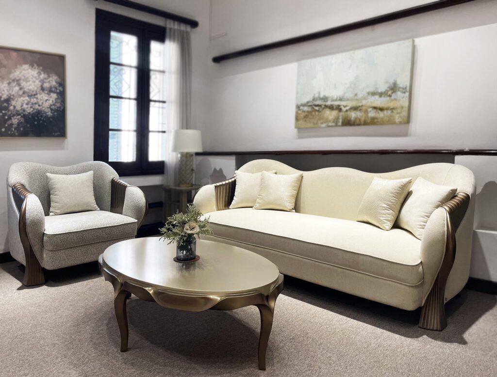 Armchair La Fonte tân cổ điển bọc vải xám nhạt, khung nâu ánh kim, đặt cạnh sofa La Fonte màu kem và bàn trà oval