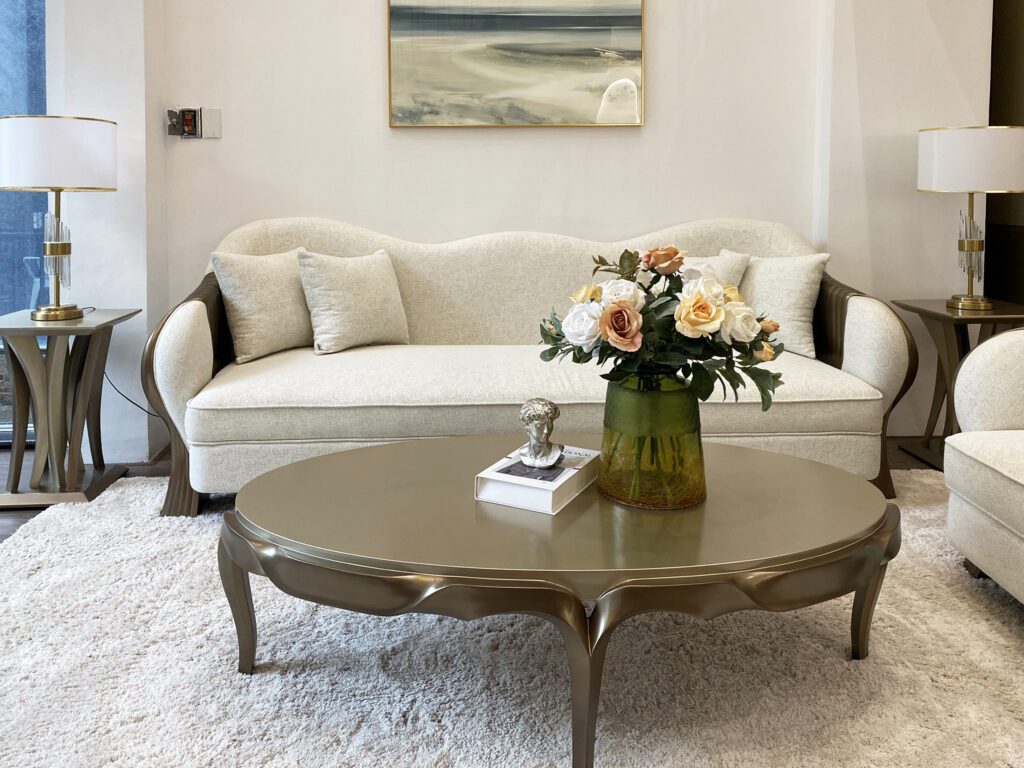 Bàn trà La Fonte tân cổ điển mặt oval liền khối màu ánh kim, chân cong, trước sofa bọc vải trắng
