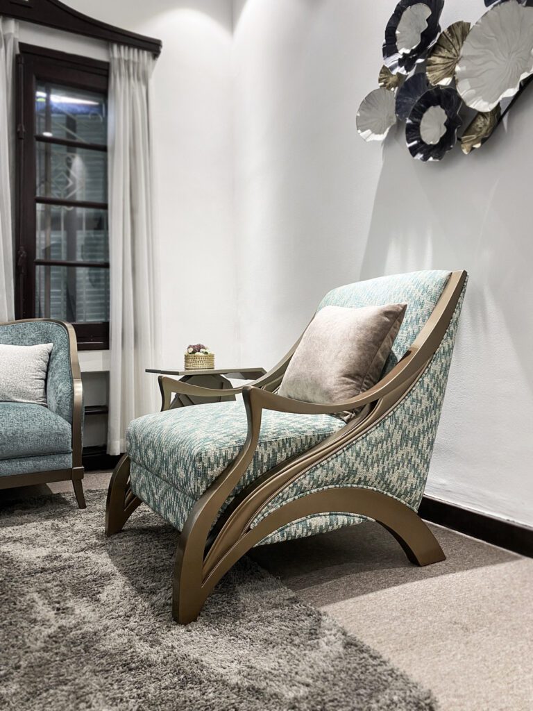 Ghế đơn Wisteria tân cổ điển bọc vải hoạ tiết xanh ngọc, tay vịn gỗ ánh kim uốn vòng chạm sàn, đặt ở góc phòng trên thảm xám
