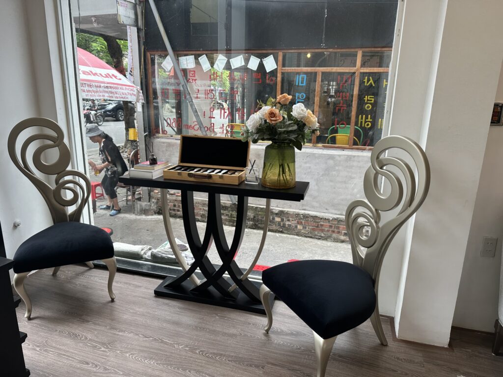 Cặp ghế đơn Accadia tân cổ điển tựa lưng cuộn xoắn sơn bạch kim, đệm đen, đặt hai bên bàn console sơn đen cạnh cửa kính